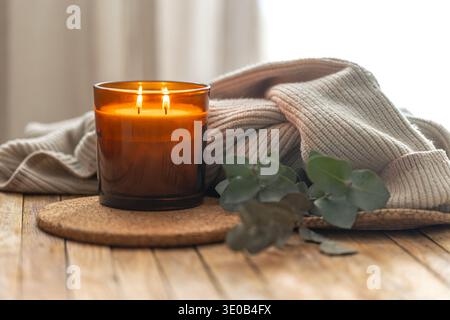 Bougie allumée dans un verre chaud avec des textures tricotées et de la verdure à la maison. Ambiance chaleureuse. Banque D'Images
