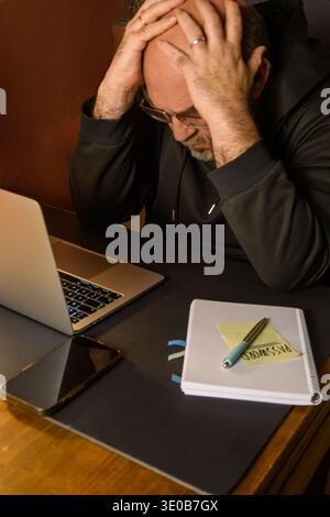 Homme stressé à un ordinateur portable avec smartphone, ordinateur portable et mot de passe note, image conceptuelle de cyber incident, problèmes de mot de passe, perte de compte et numérique Banque D'Images