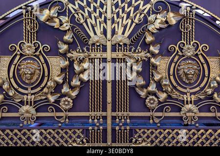 Portail en fer forgé orné de motifs lion. Gros plan détaillé d'une porte décorative en métal présentant des têtes de lion, des éléments floraux et des volutes élégantes Banque D'Images