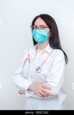 Femme médecin portant un masque de protection et stéthoscope debout avec les bras croisés, portrait professionnel de la santé représentant l'expertise médicale et Banque D'Images