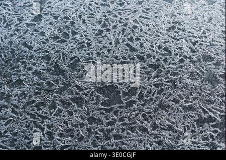 Texture en gros plan de cristaux de gel naturels formant des motifs délicats sur la glace gelée, créant un fond hivernal complexe avec des détails étincelants et Banque D'Images