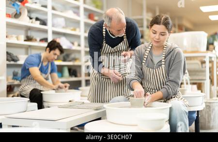 L'homme mature aide à la fille travaillant sur la roue de potier dans l'atelier de poterie Banque D'Images