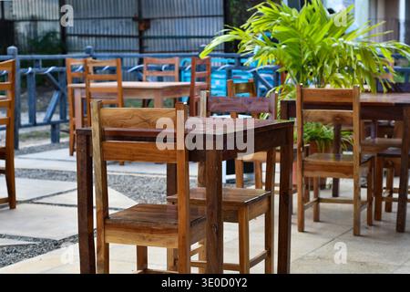 Un coin salon extérieur accueillant avec des ensembles de tables et de chaises en bois poli disposés sur un patio en pierre bien rangé. Une annonce de plantes tropicales vertes vibrantes Banque D'Images