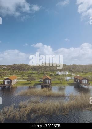 Vue aérienne des maisons sur pilotis reflétant dans les eaux tranquilles de la lagune sous un vaste ciel bleu, Praia de Mira, Coimbra, Portugal. Banque D'Images