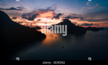 Vue aérienne des silhouettes spectaculaires des îles rencontrent le baiser ardent du coucher du soleil, peignant le ciel avec des teintes vibrantes sur la mer tranquille, El Nido, Mimar Banque D'Images