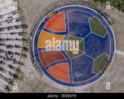 Vue aérienne d'un terrain coloré et artistique sur le thème du football, une éclaboussure vibrante de formes géométriques, entouré d'un terrain sablonneux et d'un parking à vélos, Alm Banque D'Images