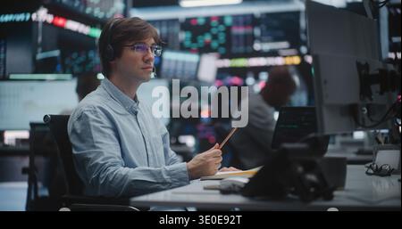 Jeune commerçant professionnel portant casque et lunettes concentre son travail et utilise Digital Tablet High Tech Workstation dans Trading Hub. Concept de Digital Asset Management, recherche en cabinet de courtage. Banque D'Images