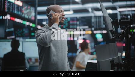 Heureux expert financier afro-américain partageant de bonnes nouvelles de croissance de portefeuille. Man Relays Investment News et Market Success Client ou collègue via smartphone. Récompenses de la gestion financière astucieuse. Banque D'Images
