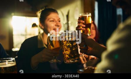 Gros plan sur un toast à la bière entre amis dans un pub lors d'une soirée décontractée Banque D'Images