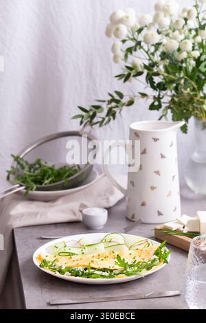 Omelette fraîchement cuite avec fromage feta et herbes, servie avec salade de radis et concombre sur une table de style ferme. Banque D'Images