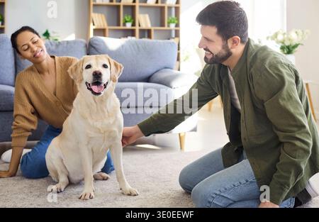 Labrador joyeux assis avec un jeune couple sur le sol dans un salon confortable lumineux Banque D'Images