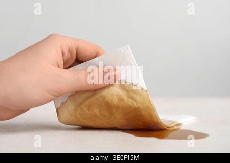Femme essuyant le café renversé avec une serviette en papier sur la table blanche grunge Banque D'Images