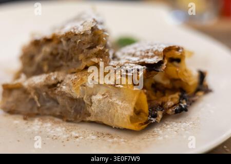 délicieuses tranches de strudel de pomme dorée saupoudrées de sucre fin en poudre sur une assiette blanche, présentant des couches de phyllo croustillantes et une garniture chaude de fruits sucrés Banque D'Images
