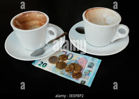 Deux tasses de cappuccino partiellement bus avec un billet et des pièces en euros sur la table. Concept de paiement dans un café pour deux personnes, rencontre autour d'un café et dépenses sociales. Banque D'Images