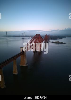 Vue aérienne en soirée du pont illuminé du Forth en Écosse avec des reflets sur l'eau calme. Monument emblématique capturé par drone au crépuscule. Banque D'Images