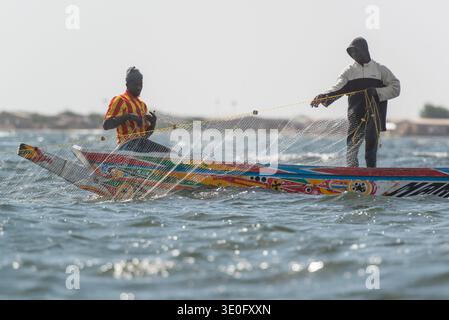 Deux pêcheurs tirent leur filet de leur bateau de pêche traditionnel en bois dans le delta du Siné-Saloum, au Sénégal. Banque D'Images