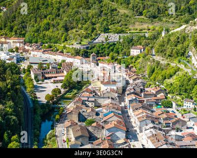 Vue aérienne du village de Saint-Rambert-en-Bugey avec des toits en terre cuite et une tour d'église à côté d'une rivière sous des collines boisées, France Banque D'Images