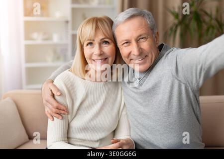 Portrait de couple senior souriant prenant selfie ensemble sur le canapé à la maison Banque D'Images