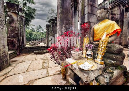 Une statue de Bouddha se dresse dans un ancien temple à Angkor, au Cambodge. Les gens placent des offrandes et de l'encens autour de la statue. Banque D'Images