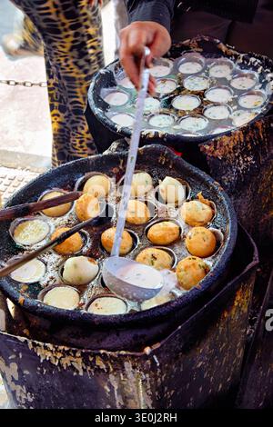 Un vendeur de rue fait de petits gâteaux ronds en utilisant une poêle spéciale dans un marché animé de Phnom Penh, au Cambodge. Le vendeur utilise une louche pour servir. Banque D'Images