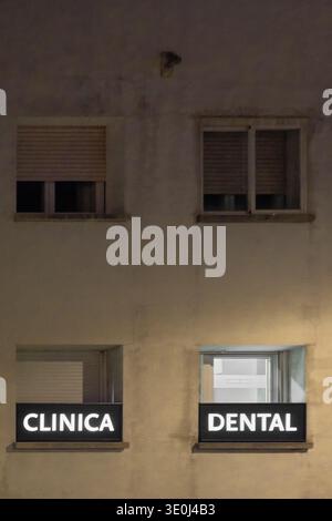 Vue extérieure d'une clinique dentaire la nuit avec texte au néon blanc brillant indiquant une pratique médicale privée dans une ville méditerranéenne. Banque D'Images