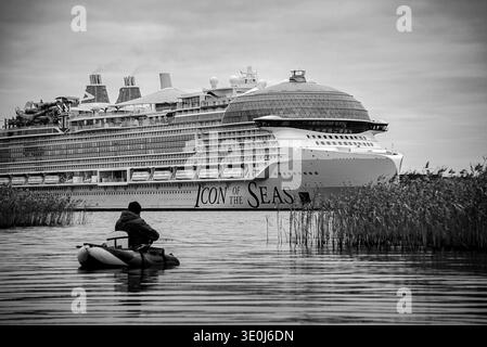 TURKU, FINLANDE - SEPTEMBRE 2023 : un pêcheur solitaire dans un tube flottant éclipsé par le plus grand bateau de croisière du monde, Icon of the Seas Banque D'Images