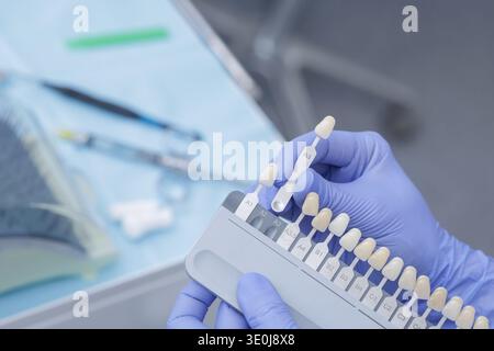 Gros plan des mains gantées tenant le guide de teinte dentaire pour correspondre à la couleur des dents avant la procédure de blanchiment dans la clinique moderne. Concept de dentisterie esthétique, sm Banque D'Images