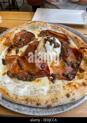 Pizza au fromage burrata, truffe et prosciutto sur croûte croustillante servie sur assiette dans un restaurant. Image adaptée au marketing de restaurant Banque D'Images