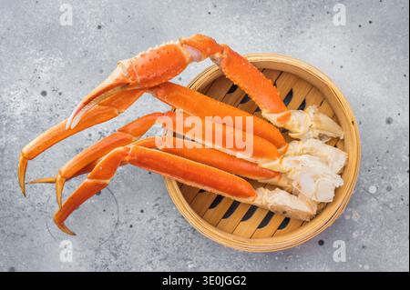Cuisses de crabe rouge kamchatka de luxe servies dans un cuiseur vapeur en bambou sur fond texturé léger composition de fruits de mer gastronomique. Banque D'Images