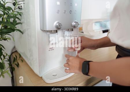 Hydratation. Femme remplissant le verre avec de l'eau du distributeur d'eau moderne. Banque D'Images