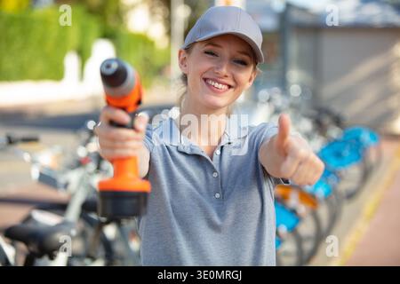 femme souriante avec perceuse montrant le pouce vers le haut Banque D'Images