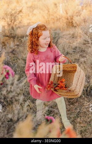 Fille rousse en robe rose à l'extérieur tenant un panier Banque D'Images