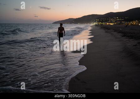 Jeune homme musclé blond marchant pieds nus sur la plage au crépuscule Banque D'Images