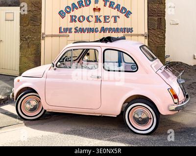 Voiture Fiat rose vintage garée devant le panneau Rocket Live Saving Apparatus sur un bâtiment en pierre Banque D'Images
