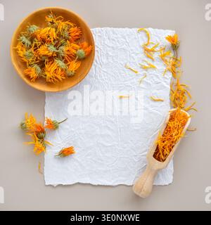Fleurs séchées de calendula dans un bol en bois et une pétales en bois avec des pétales sur papier texturé. Vue de dessus avec espace pour le texte Banque D'Images