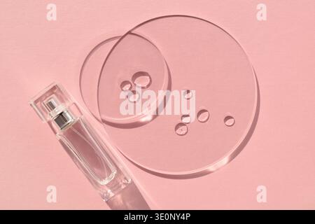 Fond rose pastel avec bouteille de parfum claire et disques transparents avec goutte dans la lumière du soleil. Vue de dessus avec espace pour le texte Banque D'Images