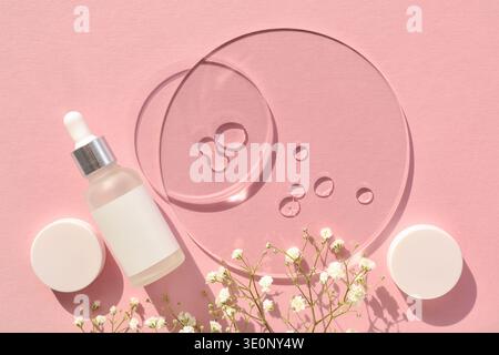 Fond rose pastel avec bouteille de sérum, gouttes de gel sur disques transparents, pot de crème et fleurs délicates. Concept de spa. Vue de dessus avec espace pour te Banque D'Images