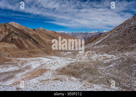 Une route de montagne sinueuse descend de Khardung la à travers une vallée aride vers la chaîne enneigée de Karakoram au loin. Banque D'Images