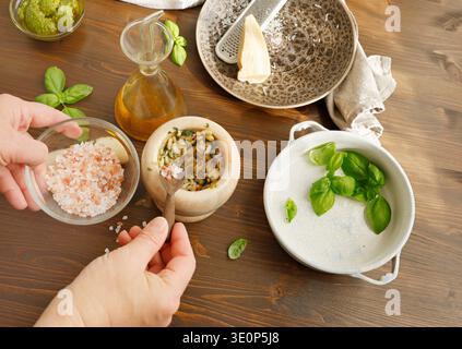 Personne ajouter le sel de mer rose au mortier de marbre tout en faisant pesto Genovese traditionnel. Gros plan des mains à l'aide d'une petite cuillère en bois pour ajouter du sel de l'Himalaya Banque D'Images