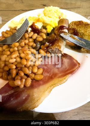 Gros plan sur une assiette traditionnelle de petit-déjeuner cuisiné avec bacon, haricots, saucisses et œufs brouillés Banque D'Images