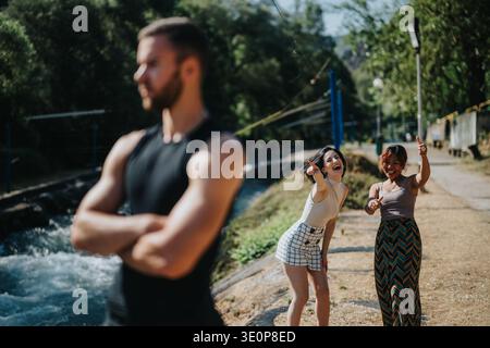 Trois amis profitent d'un moment ensoleillé en plein air au bord de la rivière, en ondulant et en souriant Banque D'Images