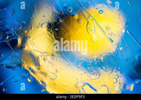 Plan macro artistique de liquides bleus et jaunes tourbillonnants avec bulles d'air et effet bokeh doux créant une sensation d'énergie et de mouvement fluide. Banque D'Images