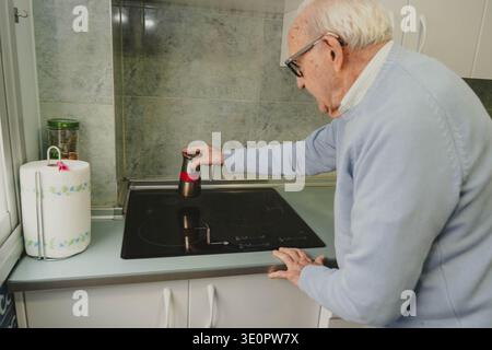 Homme âgé plaçant un pot de moka sur une table de cuisson à induction dans sa cuisine Banque D'Images