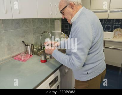 Homme âgé remplissant un pot de moka avec de l'eau à l'évier de la cuisine Banque D'Images