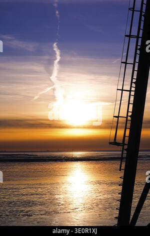 Vue du coucher de soleil sur la mer avec échelle et ciel dramatique dans des couleurs chaudes, échelle en métal du monument phare Obereversand et un coucher de soleil sur le Banque D'Images