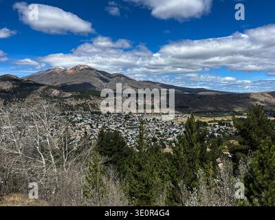 Vue panoramique surélevée sur la ville d'Esquel en Patagonie Argentine, entourée d'arbres verdoyants au premier plan et de chaînes de montagnes spectaculaires. Banque D'Images
