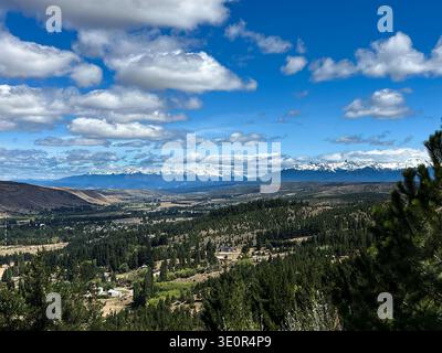 Vue panoramique surélevée sur la ville d'Esquel en Patagonie Argentine, entourée d'arbres verdoyants au premier plan et de chaînes de montagnes spectaculaires. Banque D'Images