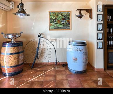 Venets, Bulgarie - 08 octobre 2024 : intérieur rustique de la cave présentant des tonneaux en bois, un vélo vintage et des œuvres d'art encadrées sur le mur avec certific Banque D'Images