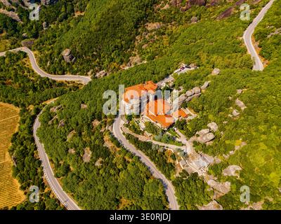 Vue aérienne du monastère perché sur un éperon rocheux, entouré de forêts verdoyantes et de routes sinueuses, Météores, Trikala, Grèce. Banque D'Images