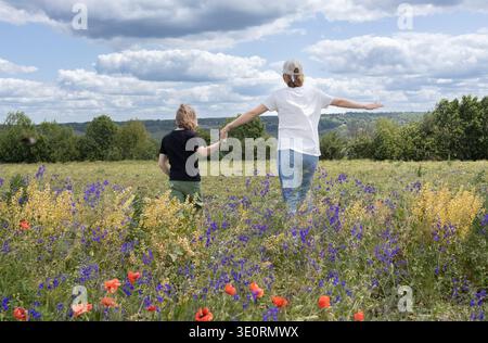 enfant et femme méconnaissables, une mère et un fils, courent à travers un pré fleuri Banque D'Images